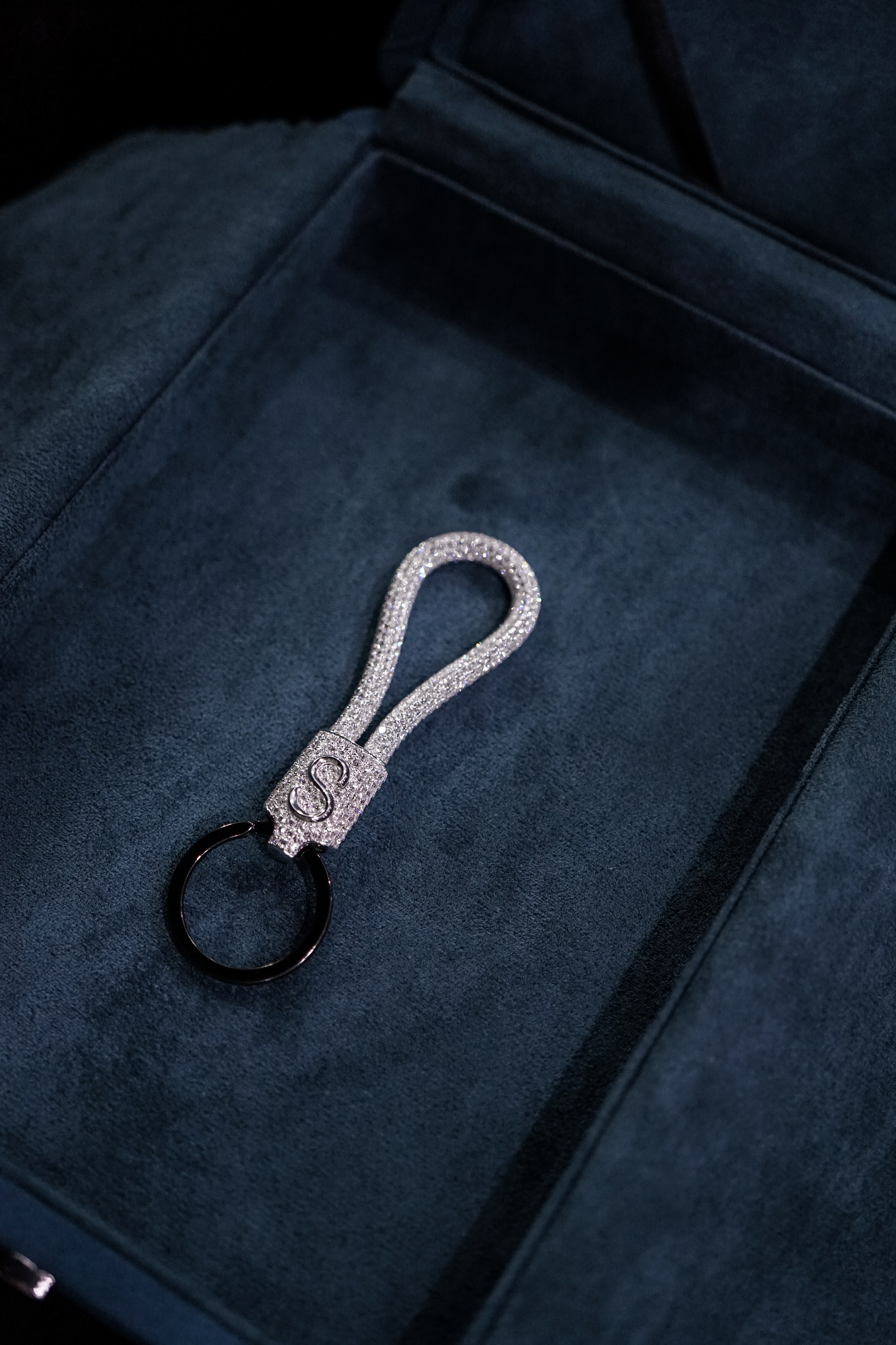 A luxurious keychain featuring a sparkly, encrusted loop and a sleek black ring, set against a dark blue velvet background.