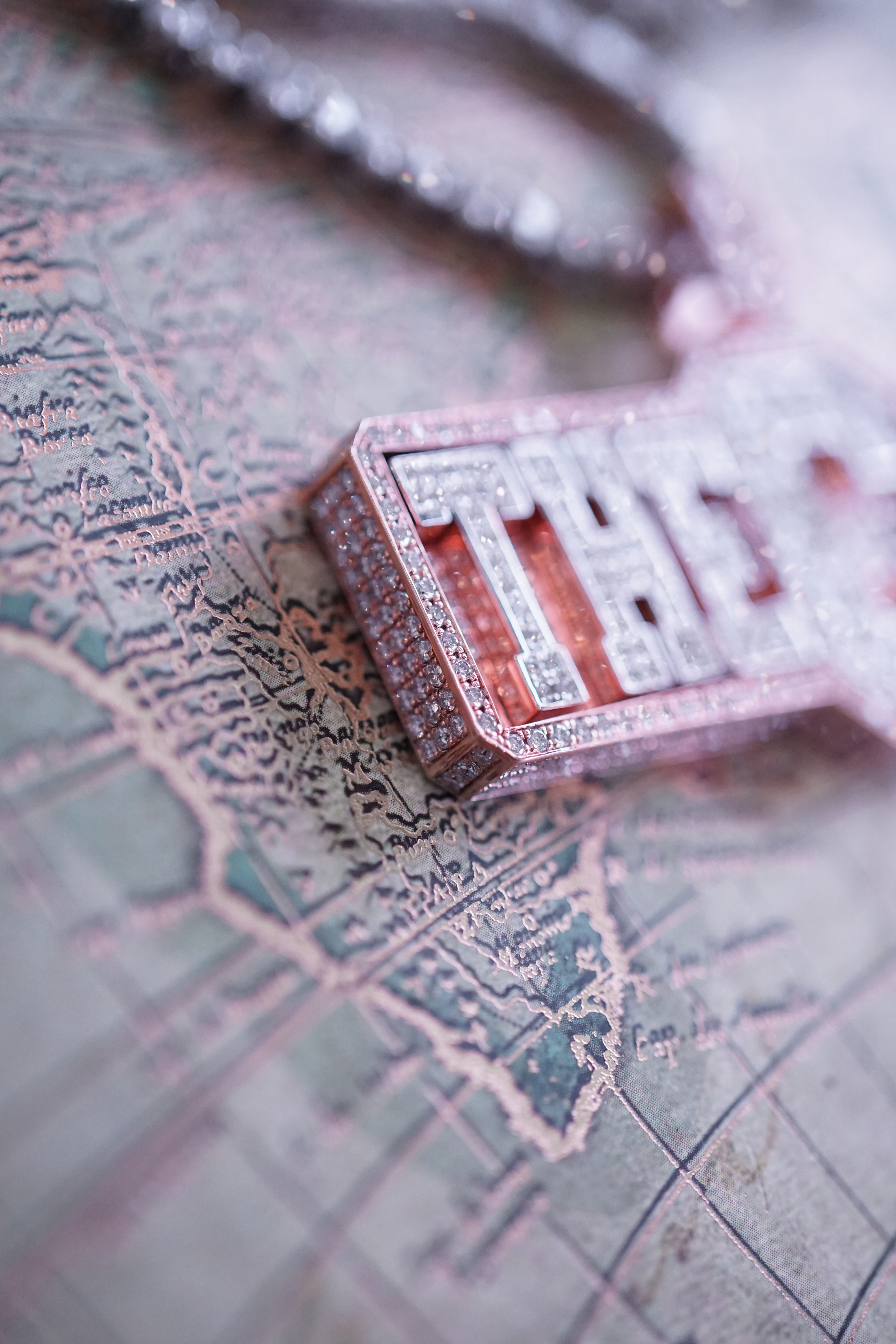 Close-up of a diamond-studded necklace with the word 'THE' resting on an intricate map background.
