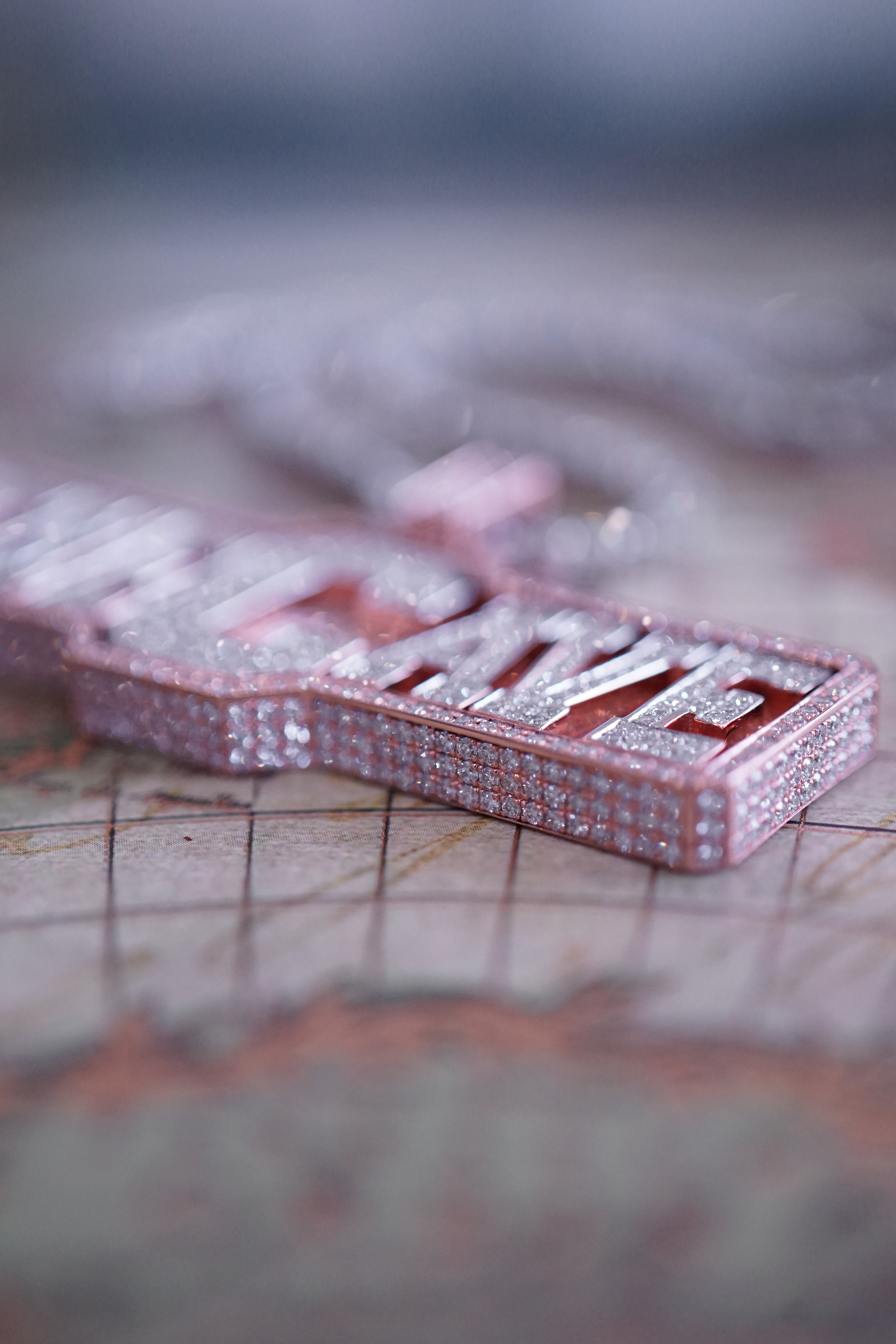 Close-up of a pink diamond-encrusted pendant shaped like a keychain with the word 'SAVE' prominently displayed.