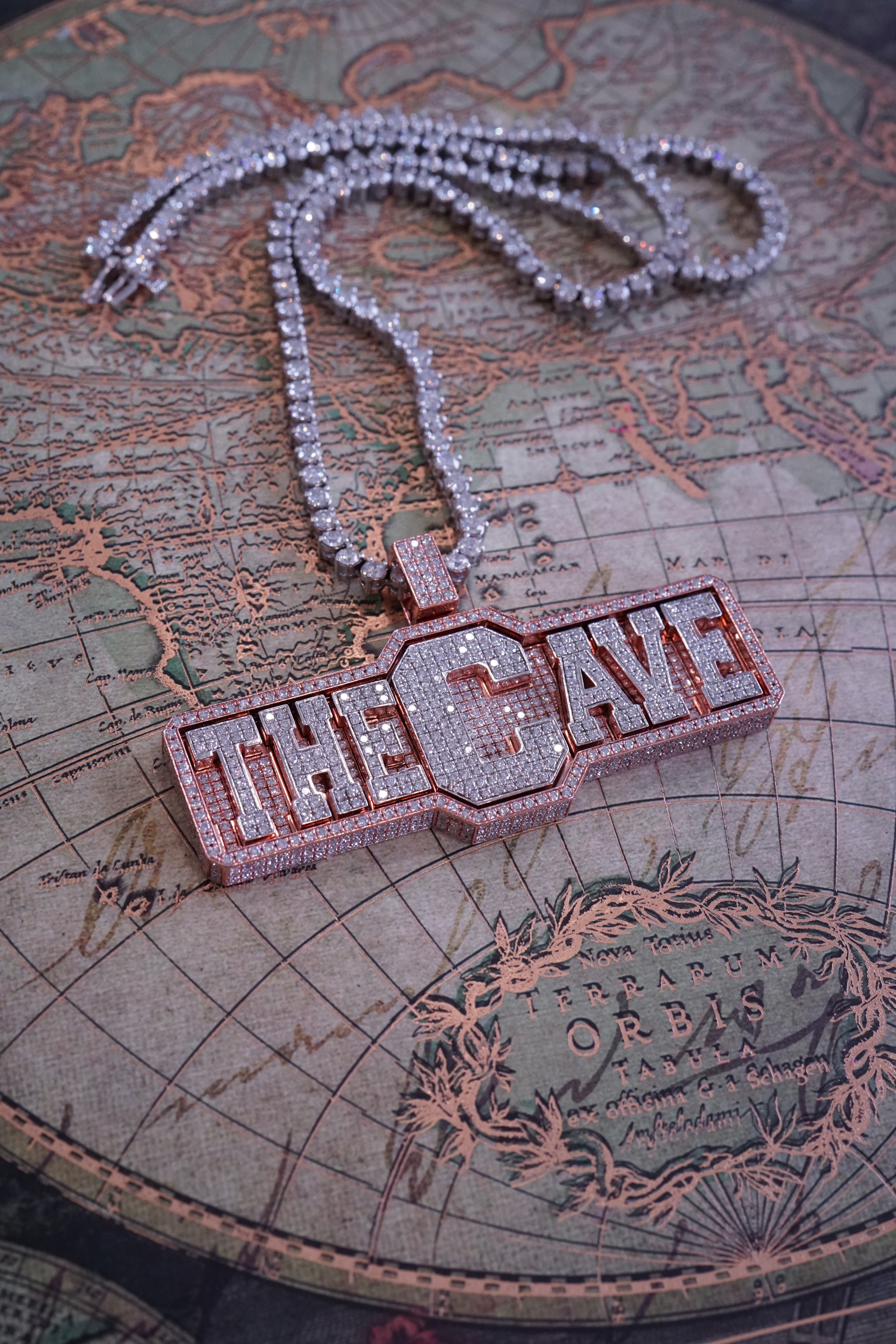 Close-up of a diamond-encrusted necklace featuring a pendant that reads 'THE CAVE,' laid on a vintage map.